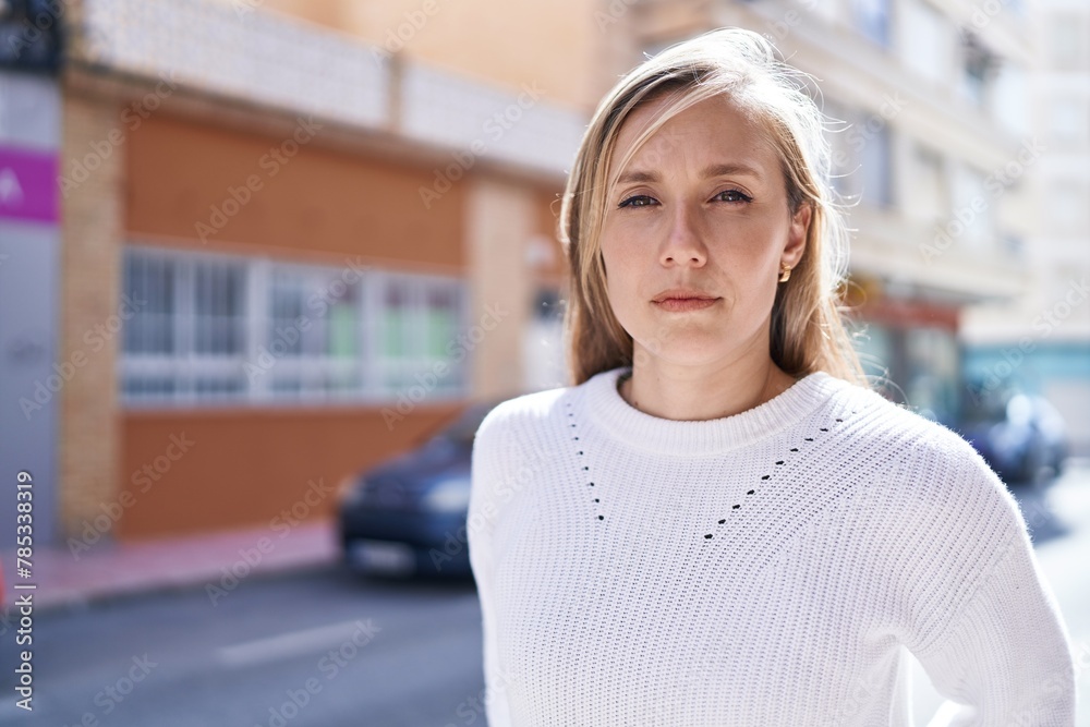 Young blonde woman standing with serious expression at street Young blonde woman standing with serious expression at street