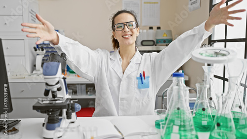 Happy scientist woman celebrating success in lab filled with glassware and microscope.