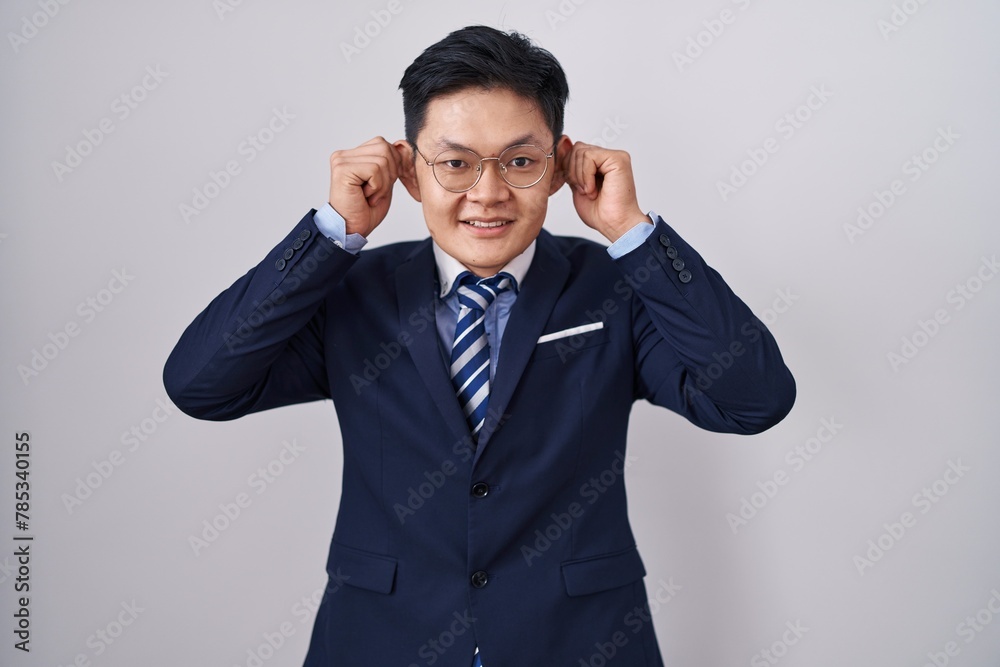 Young asian man wearing business suit and tie smiling pulling ears with fingers, funny gesture. audition problem Young asian man wearing business suit and tie smiling pulling ears with fingers, funny gesture. audition problem