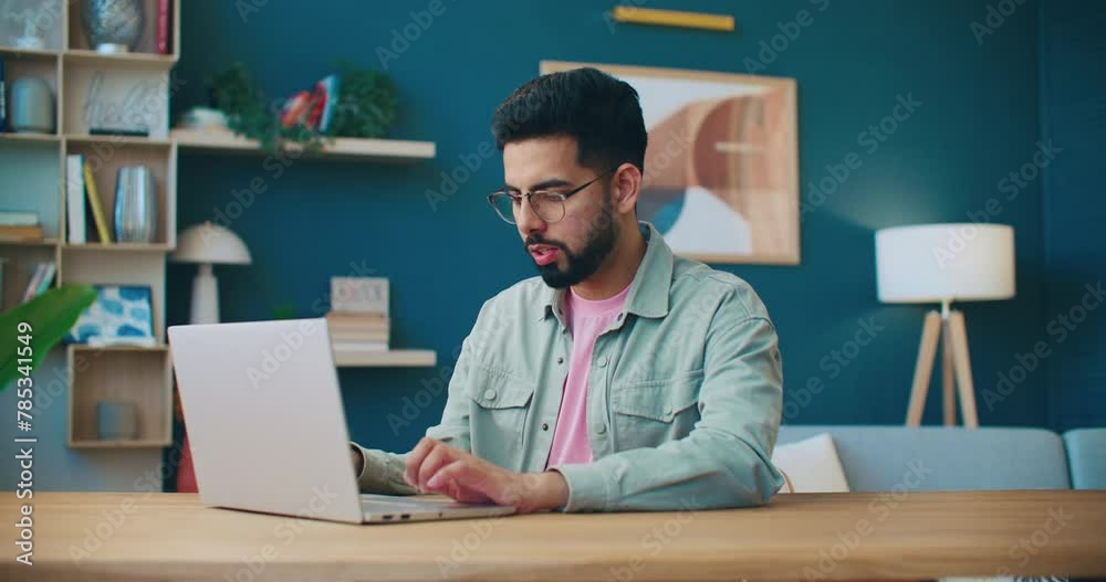 Man working with laptop. Male sitting at table and closing laptop. Man working at home office. Smiling man wearing glasses. Cozy flat. Male freelancing at home. Man satisfied with finishing work.
