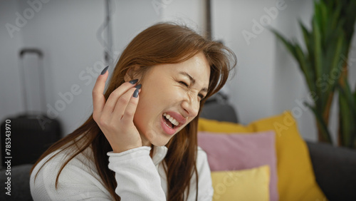 A young caucasian woman in pain, holding her ear, expressing discomfort in a modern living room setting.