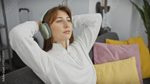 A relaxed young woman enjoys music with headphones in a cozy living room interior.