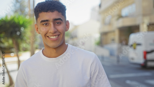 A young man smiles as he stands outdoors in an urban city setting, capturing a sense of youthful vitality and casual urban life. © Krakenimages.com