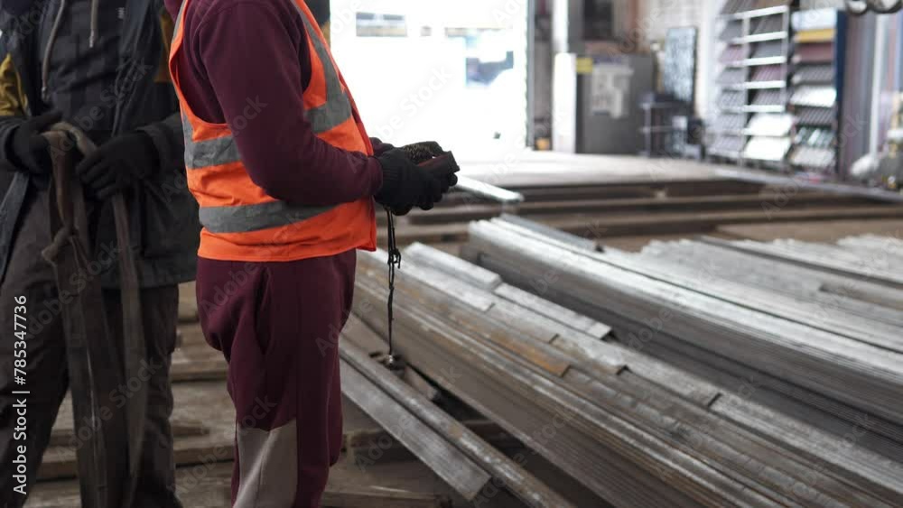 A worker moves large industrial metal parts using a remote control overhead rack crane. Heavy industry for manufacturing metal structures.