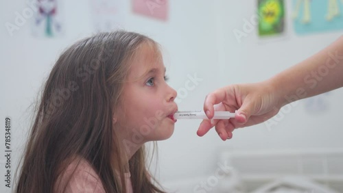Caring mother giving medicines to her daughter with oral syringe. Hand of mother inject medicine antibiotic with syringe in mouth of little child girl during cold with bacterial infection.