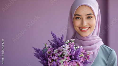 A beautiful woman in hijab holding a bouquet of purple flowers.