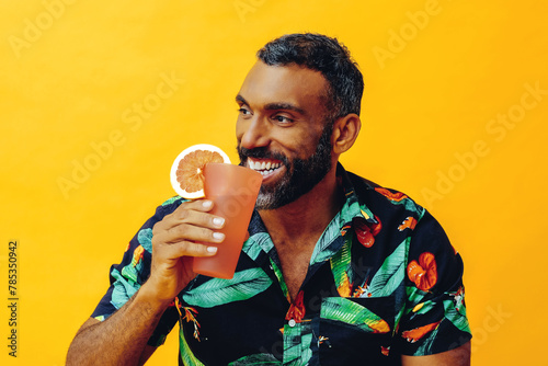 handsome bearded mid adult african american man smiling on vacation sitting on a chair drinking orange juice cocktail