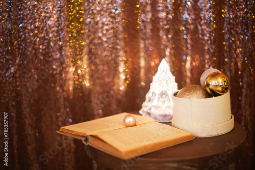 Little box with a lot of Christmas silver and golden decorations near the Christmas tree lamp and the book