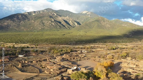 Beautiful drone view of Taos old town in New Mexico, USA, with the mountains in the back and a cloudy autumn day with golden light.
