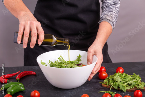 A cook pouring olive oil on a fresh vegetable salad with tomatoes and arugula, closeup with selective focus