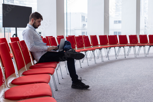 Portrait d'un homme qui travaille seul, assis dans une salle de réunion ou une salle de conférence avec un ordinateur portable. C'est un homme d'affaires ou un salarié d'une entreprise photo