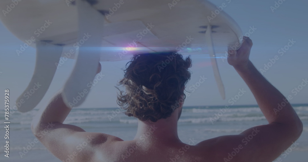 Fototapeta premium Image of lights over back view of caucasian surfer on beach