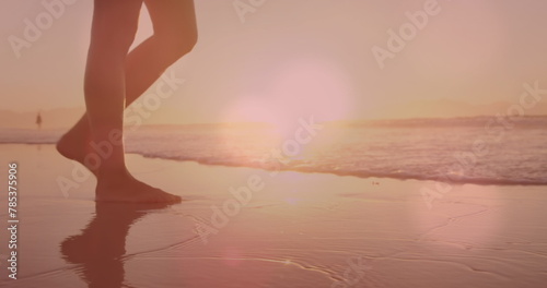 Image of lights over legs of caucasian woman walking on beach