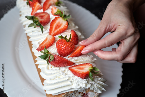 girl decorates a cream roll with fresh strawberries
