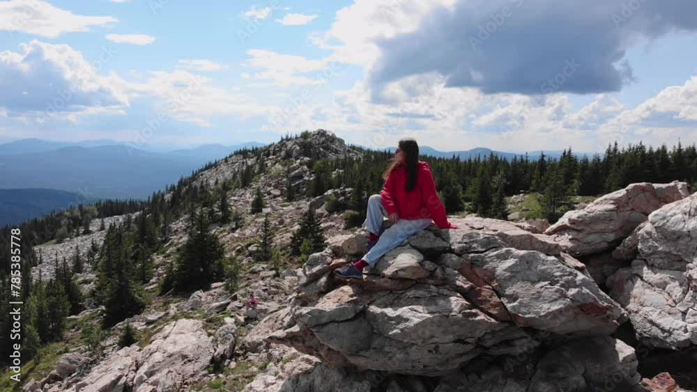 A young girl, wearing a red hoodie and glasses, enjoys a beautiful view of the rocky mountains surrounded by forests. Aerial footage. 4k A young girl, wearing a red hoodie and glasses, enjoys a beautiful view of the rocky mountains surrounded by forests. Aerial footage. 4k