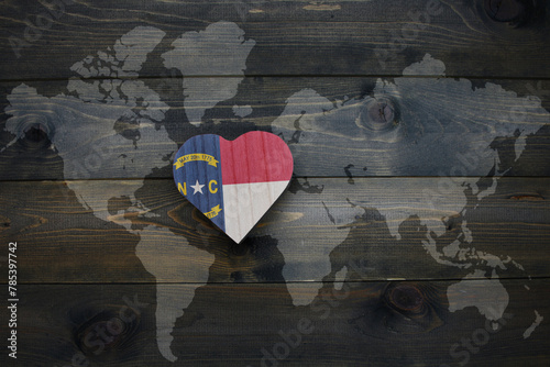 wooden heart with national flag of north carolina state near world map on the wooden background.