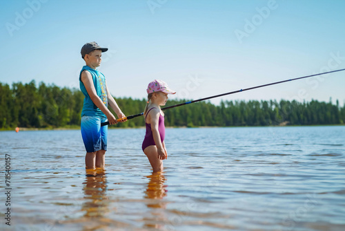 kids fishing standing in the lake. Boy holding a long fish rod