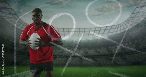 Image of an African American male rugby player standing, playing with a ball and looking to camera w © vectorfusionart