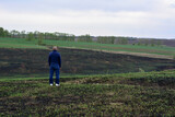 a man in a blue jacket is standing and looking at a burnt field 