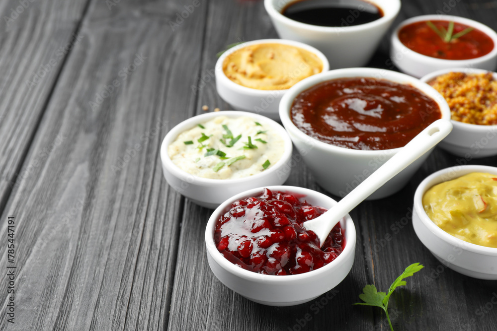 Different tasty sauces in bowls and parsley on black wooden table, closeup. Space for text
