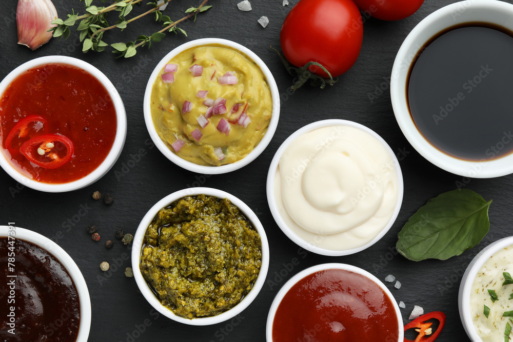 Different tasty sauces in bowls and ingredients on black table, flat lay Different tasty sauces in bowls and ingredients on black table, flat lay