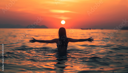The elegant girl in the sea with her arms open to the sun that is setting