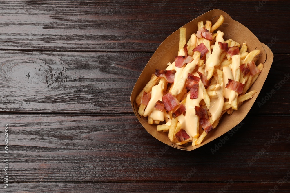 Tasty potato fries, cheese sauce and bacon in paper container on wooden table, top view. Space for text Tasty potato fries, cheese sauce and bacon in paper container on wooden table, top view. Space for text