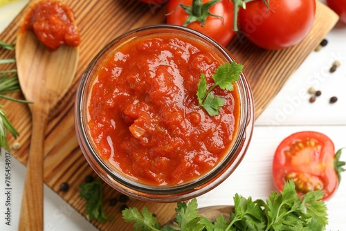 Homemade tomato sauce in jar, spoon and fresh ingredients on white wooden table, flat lay