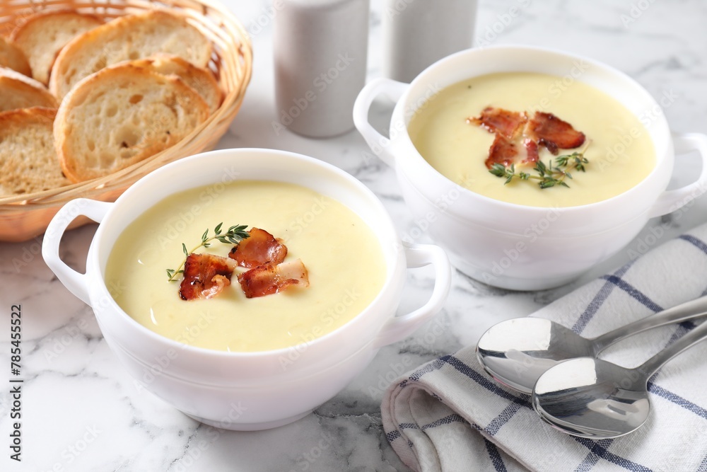 Tasty potato soup with bacon and rosemary in bowls served on white marble table Tasty potato soup with bacon and rosemary in bowls served on white marble table