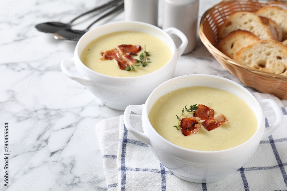Tasty potato soup with bacon and rosemary in bowls served on white marble table Tasty potato soup with bacon and rosemary in bowls served on white marble table
