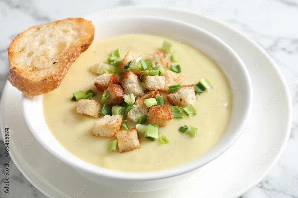 Tasty potato soup with croutons and green onion in bowl on white marble table