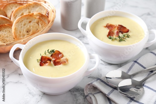 Tasty potato soup with bacon and rosemary in bowls served on white marble table