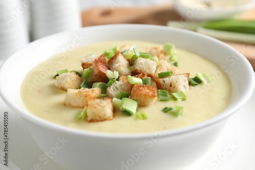Tasty potato soup with croutons and green onion in bowl on white table, closeup