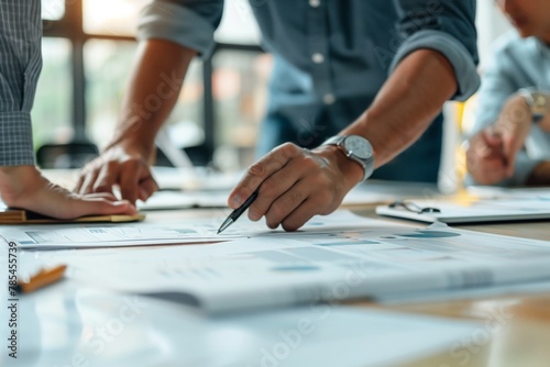 A close-up view captures the essence of teamwork in a professional setting, focusing on the hands of a person pointing with a pen at business documents.