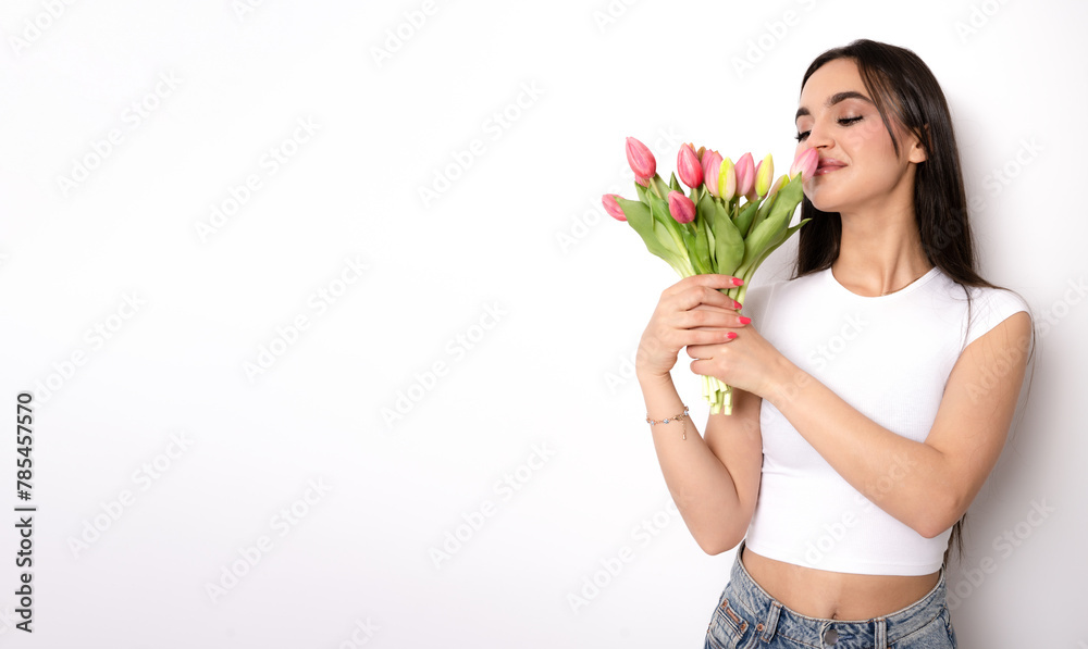 Young woman in casual outfit holds bouquet of pink tulips and smells them on white isolated background Young woman in casual outfit holds bouquet of pink tulips and smells them on white isolated background