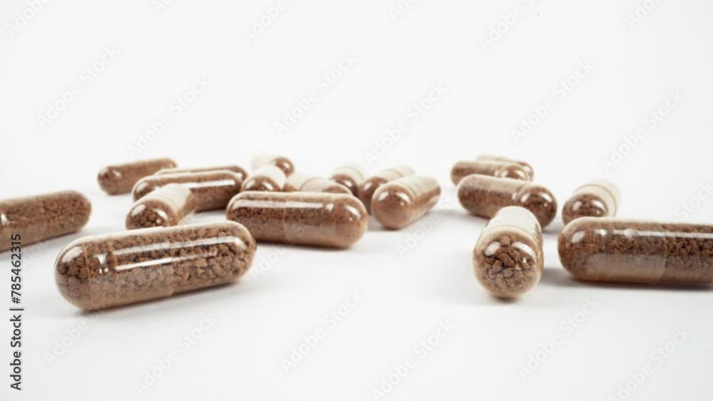 Close-up of brown herbal supplements in clear capsules scattered on white Close-up of brown herbal supplements in clear capsules scattered on white