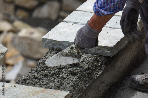 muratore al lavoro cazzuola cemento costruzione muro di sassi pietre  photo