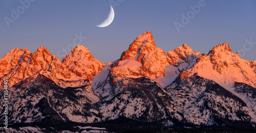 Sunrise on Teton Mountain Range in Wyoming Alpen Glow Orange and Pink on Rugged Mountains with Crescent Moon photo