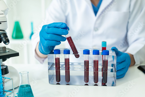 Hospital doctor holds blood vessel test in laboratory with blood sample from shelf with analyzer in lab