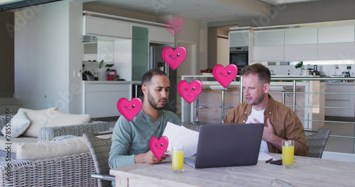 Image of heart icons over diverse gay couple using laptop