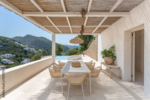 Large terrace with a dining table and outdoor kitchen, covered by a thatched roof in the style of white concrete architecture. Ibiza landscape. Pool.