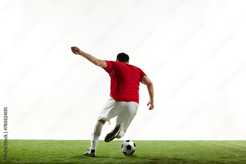 Fototapeta premium Man, football player in motion during game training, running on filed with ball isolated on white background. Concept of professional sport, game, competition, tournament, action. Back view