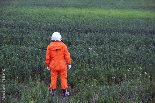 Rear view of man wearing orange astronaut space suit and space helmet standing in green grass outdoors. Travel concept