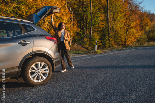 a smiling man with a backpack on his back closes the trunk of the car in autumn season. copy space