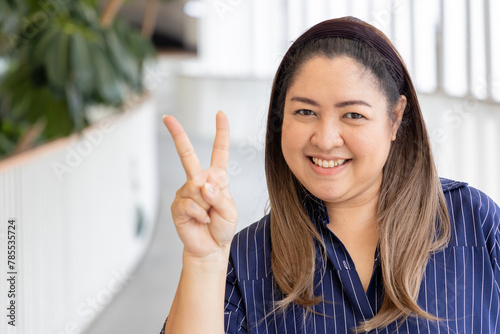 Happy smiling middle aged asian woman pointing 2 fingers up, concept of v for victory, two points, number two, second point