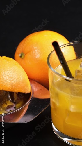 bicchiere con spremuta d'arancia e ghiaccio, cannuccia nera, spremiagrumi con buccia di arancia, video verticale photo