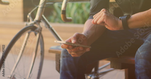 Image of biracial man sitting and using smartphone with bicycle