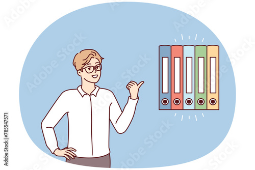Man office worker points finger at multicolored folders for documents. Guy in business clothes gives advice on finding reports or recommends system for storing financial papers