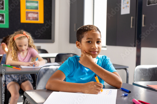 In school, young biracial male student sitting at a desk in a classroom, looking thoughtful