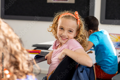 Wallpaper Mural In school, young Caucasian girl with curly hair is smiling, sitting at a desk in a classroom Torontodigital.ca